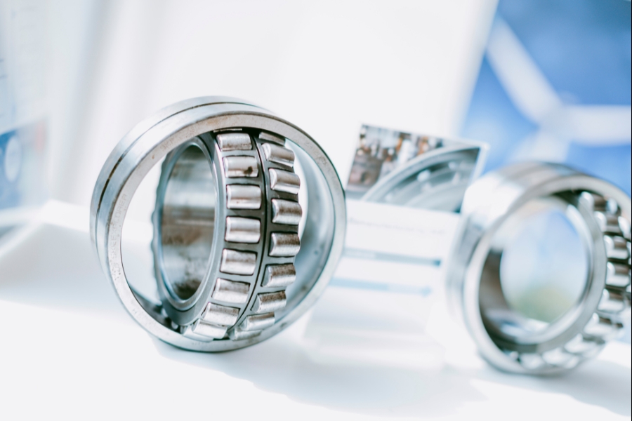 Nahaufnahme zweier Pendelrollenlager auf einer weißen Fläche. Die Lager bestehen aus glänzendem Metall mit sichtbaren Rollen. Der Hintergrund ist leicht verschwommen und weist einen Hauch von Blau und Weiß auf.